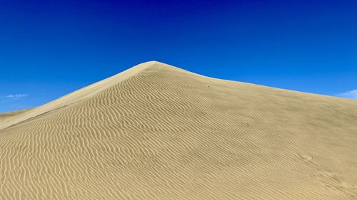 Low angle view of sand dunes against clear blue sky