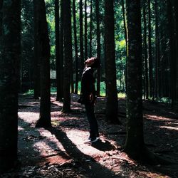 Side view of man standing by trees in forest