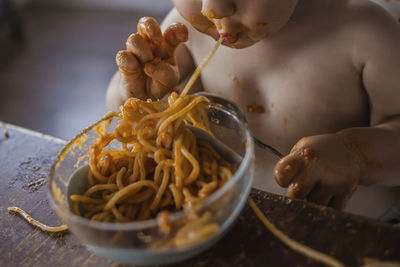 Midsection of shirtless baby boy eating noodles while sitting at home