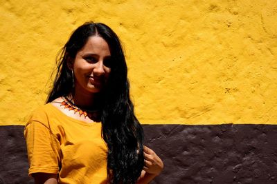 Portrait of smiling young woman against yellow wall