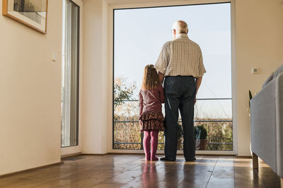 Grandfather and granddaughter looking out of window, rear view