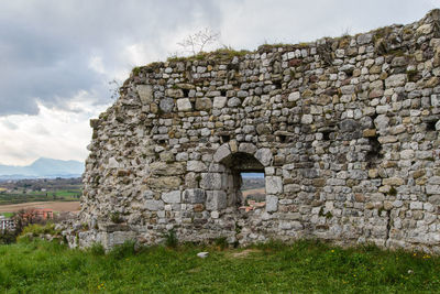 Stone wall of old building against cloudy sky