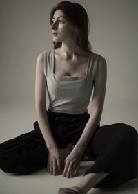 Woman looking away while sitting against beige background