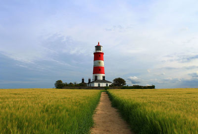 Trail on grassy field leading towards happisburgh lighthouse against cloudy sky