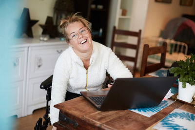 Portrait of smiling disabled woman using laptop at table in house