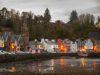 Illuminated buildings by lake against sky at dusk