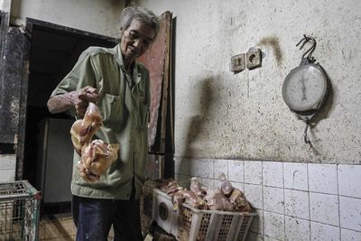 Senior man holding chicken in butcher shop