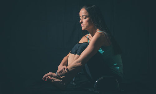 Mid adult woman with exercise equipment while sitting against black background