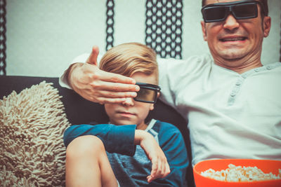 Father and son eating popcorn while watching movie at home