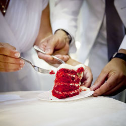 Midsection of bride and groom holding cake slice in plate