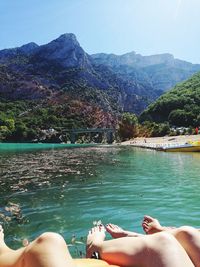 Low section of woman relaxing by lake against mountains