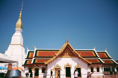 People outside temple against clear blue sky