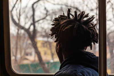 Rear view of man looking through window while sitting in bus