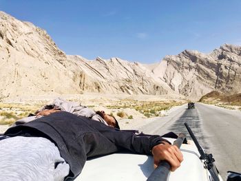 Man lying on car against mountain