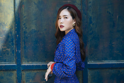 Woman looking away while standing against blue wall