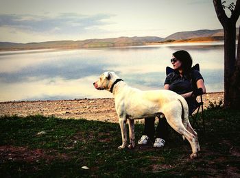 Young woman with dog sitting at lake against sky