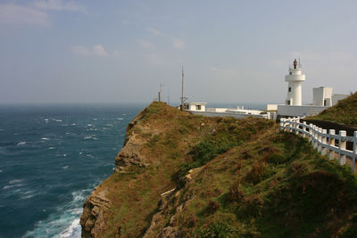 Lighthouse amidst sea and buildings against sky