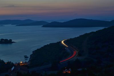 High angle view of light trails on road by sea at dusk