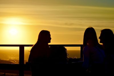 Side view of silhouette friends sitting on chairs at sunset