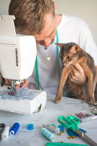 Sewing clothes for pets. tailoring clothes for cats. a smiling seamster is sewing for abyssinian cat