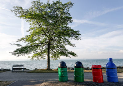 Garbage can on road by lake against sky