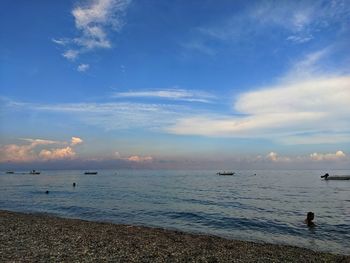 People in sea against sky during sunset