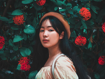 Portrait of young woman in hat standing against plants