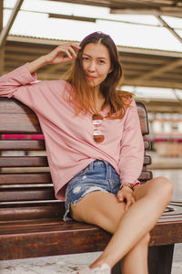 Portrait of woman sitting on bench at railroad station platform