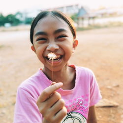 Portrait of smiling girl holding dandelion outdoors