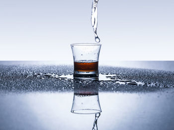 Water pouring in glass on table with reflection against white background