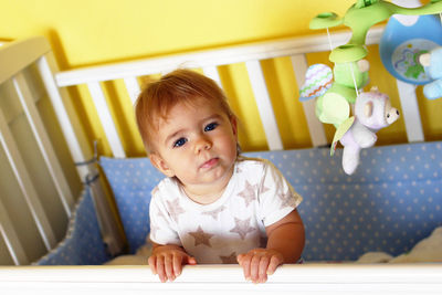 Cute one year old girl with blue eyes and blond hair just woke up in the morning in her bed.