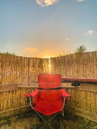 Empty chairs by plants against sky during sunset