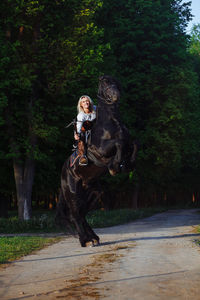 Portrait of smiling young woman with cross bow riding horse on road