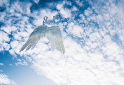 Double exposure image of costume wings flying against cloudy sky