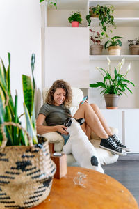 Portrait of young woman sitting on potted plant at home