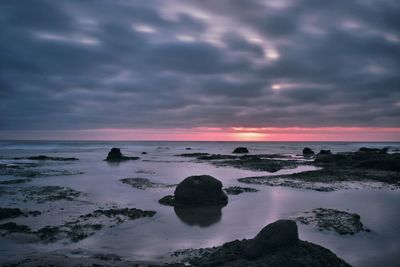 Rocks at seashore against cloudy sky during sunset