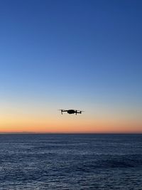 Airplane flying over sea against clear sky during sunset