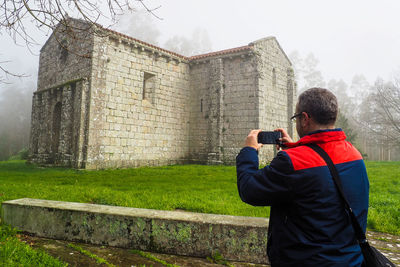Rear view of man photographing against built structure