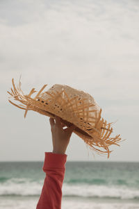 Cropped hand holding hat against sky