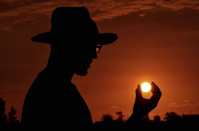 Silhouette of young woman standing against orange sun