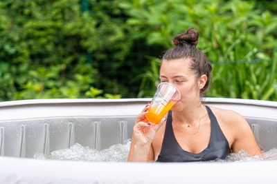 Gorgeous teenage girl with long, dark hair and glass with drink in the garden inflatable pool