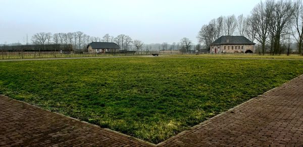 Scenic view of grassy field by houses against sky