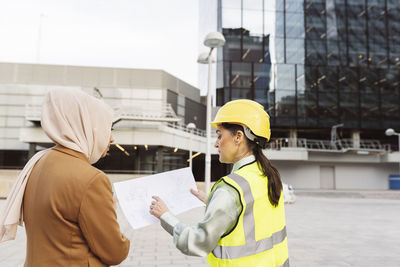 Architect discussing over blueprint with businesswoman outside modern building