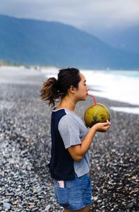 Woman drinking coconut water while standing at beach