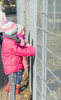 Side view of girls wearing warm clothing looking through fence