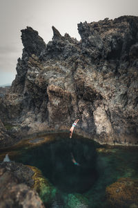 Full length of man jumping in pond from rocky mountain