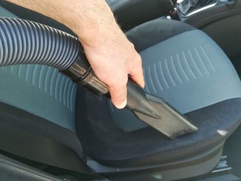 Cropped hand of man cleaning vehicle seat with vacuum cleaner in car