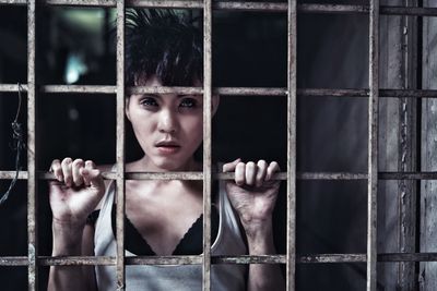 Portrait of woman standing by metal grate