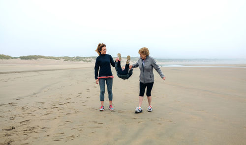 Women playing with daughter at beach against sky