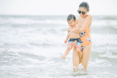 Smiling mother with son enjoying on sea water